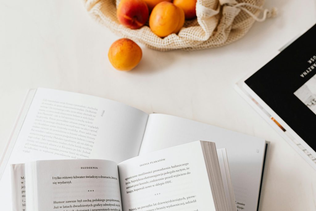 Top view of open books on a table with apricots in a net bag, indoors.