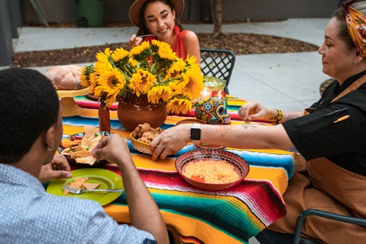 Group of adults enjoying a colorful outdoor meal with sunflowers on the table.