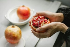 A close-up of hands peeling a ripe pomegranate indoors, showcasing vibrant red seeds.