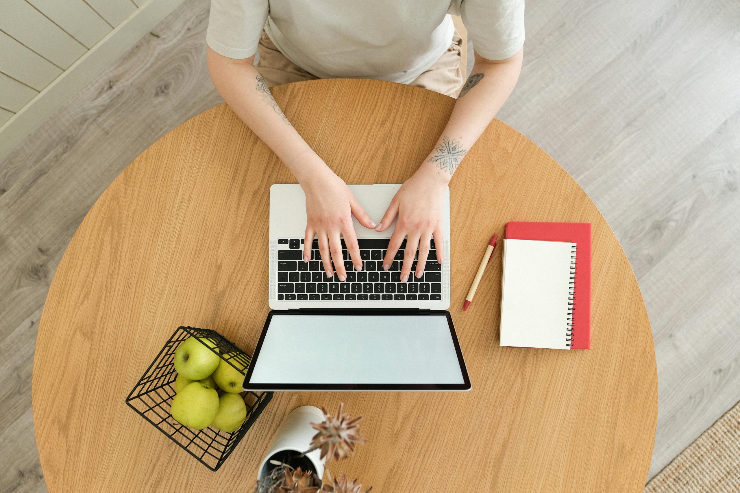 Overhead view of a workspace setup with laptop, notebook, and apples, perfect for remote working scenarios.